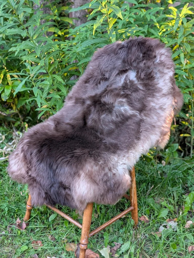 A plush natural brown and gray british isles sheepskin rug draped over a wooden chair for cozy decor