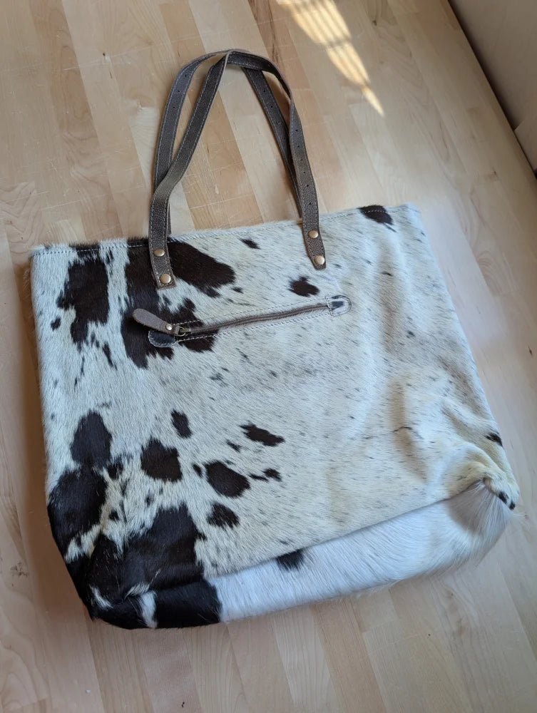 A white and black real cowhide tote bag with brown leather handles perfect for everyday use