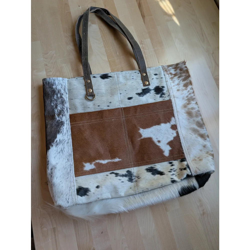 A rustic real cowhide tote bag with black and white patchwork and a brown suede stitched front pocket panel