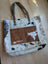 A rustic real cowhide tote bag with black and white patchwork and a brown suede stitched front pocket panel