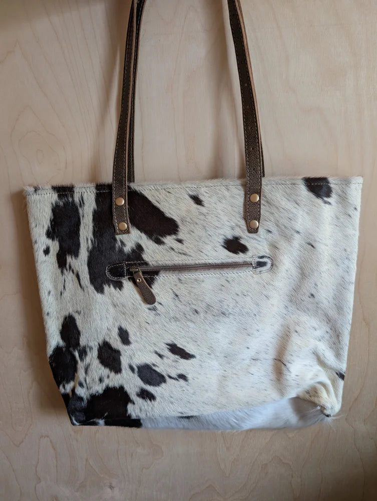 White and black real cowhide tote bag with brown leather straps perfect for carrying essentials like real cowhide rugs fans