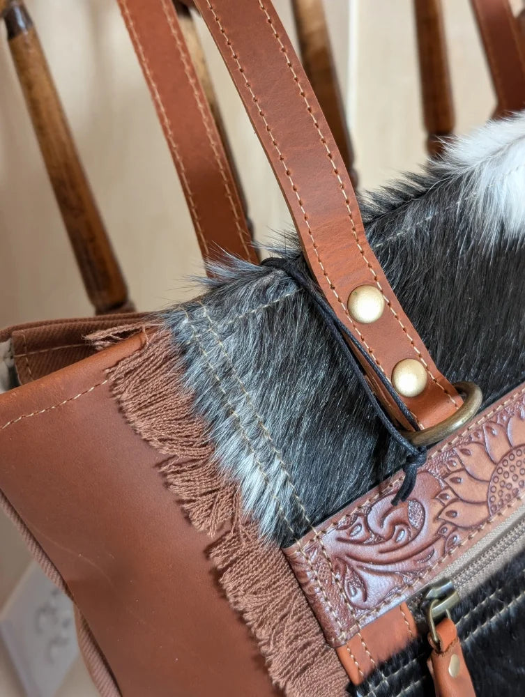 Brown leather oakley bag with real cowhide black and white trim, fringed detailing, and embossed floral zipper pull