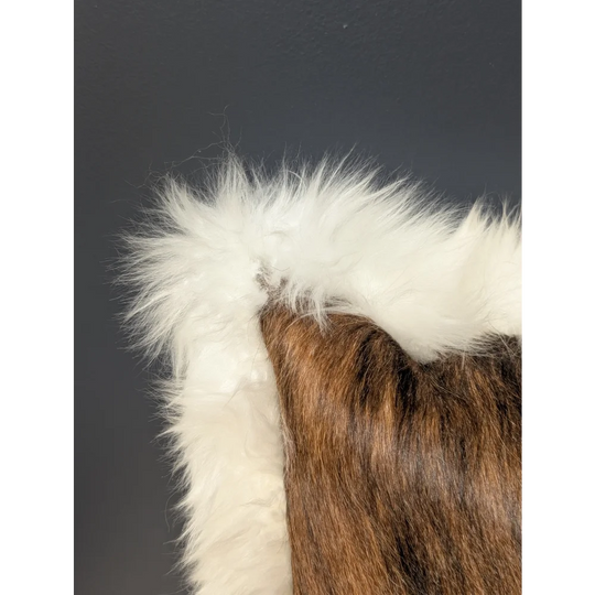 A plush, rich brown and white merino sheepskin cushion by angus oliver made in canada with a cozy fuzzy texture