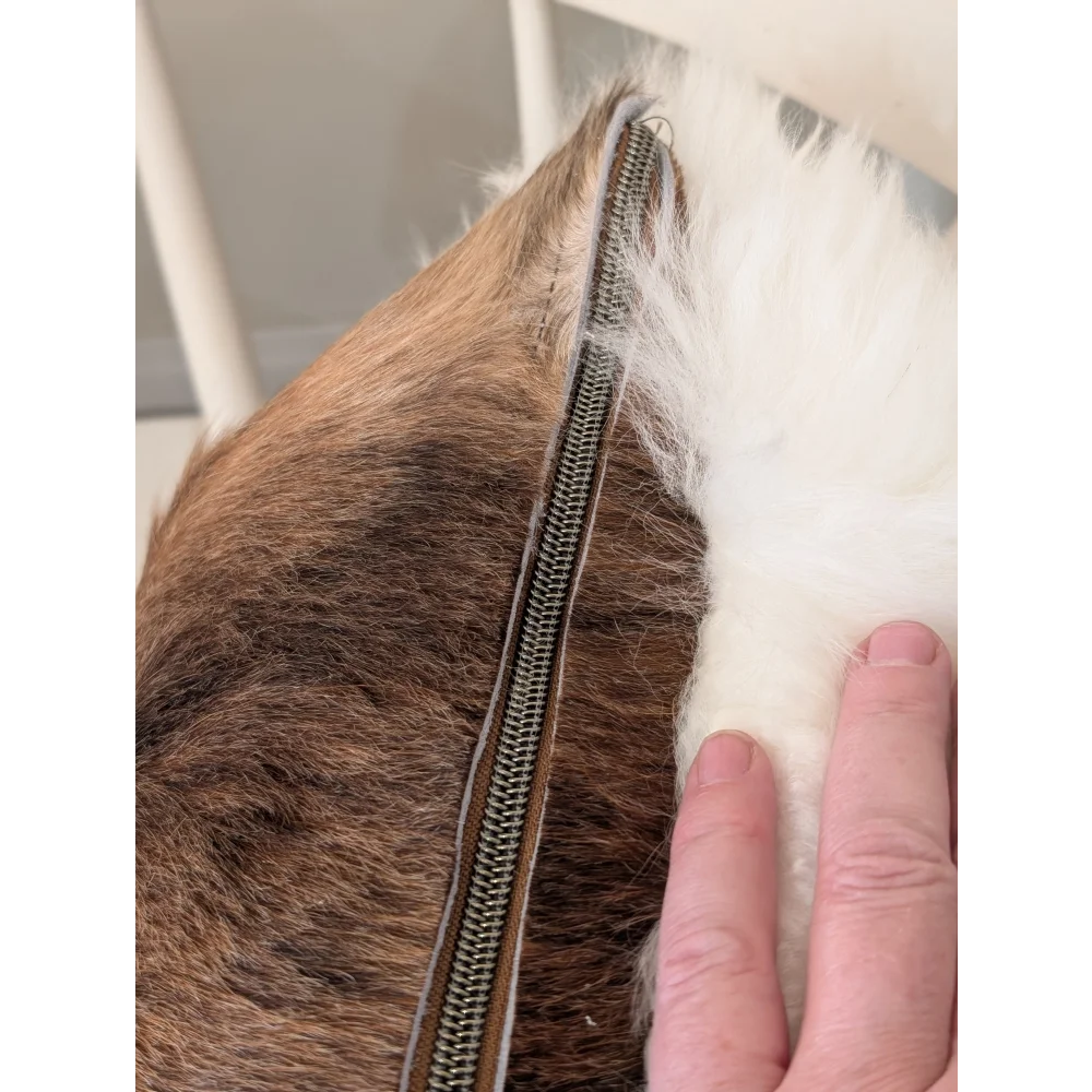 A one of a kind merino sheepskin cushion by angus oliver canada with a metallic zipper splitting brown and white fur