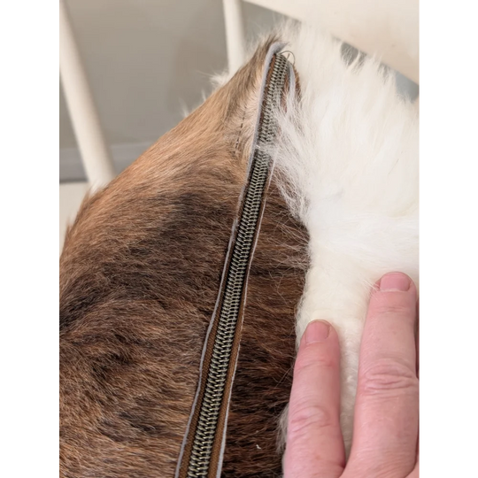 A one of a kind merino sheepskin cushion by angus oliver canada with a metallic zipper splitting brown and white fur