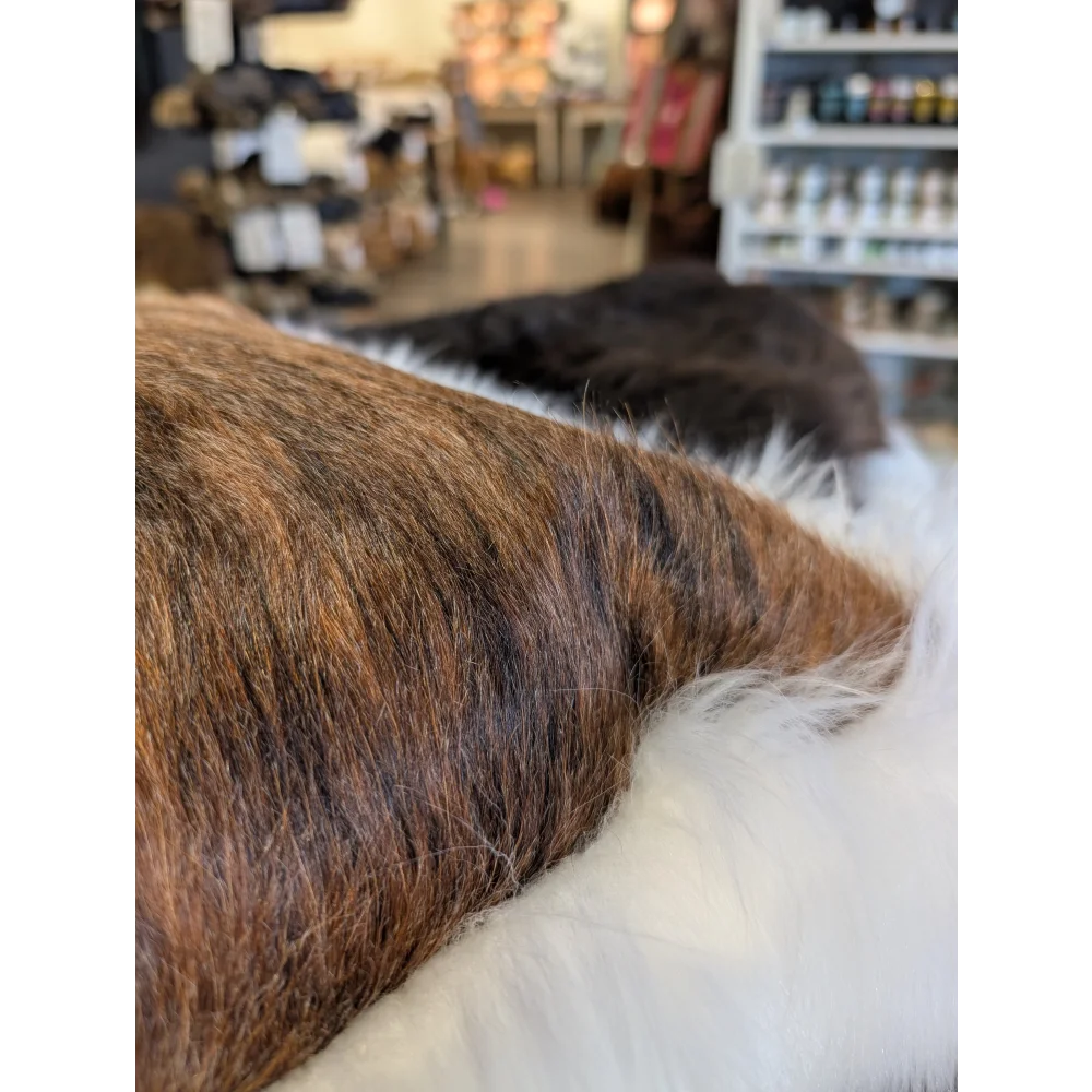 Close-up of the back of an angus oliver canada brown and black cowhide merino sheepskin cushion resting on white faux fur