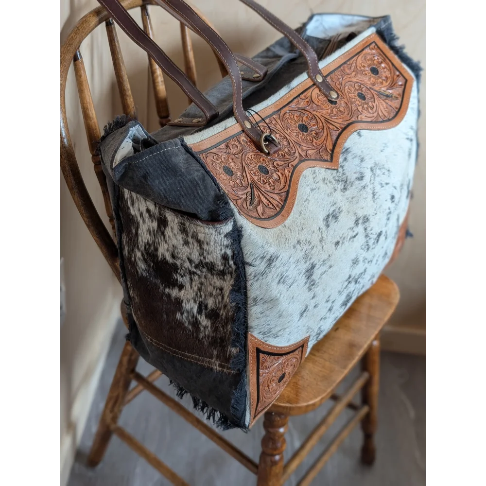 The sunflower weekender bag is a rustic cartwright hand-tooled bag with white and brown hair-on hide and a zippered pocket