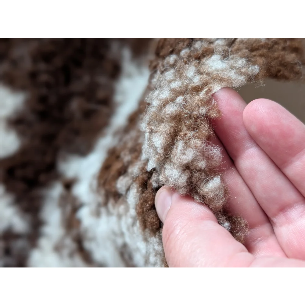 A hand gently holds a soft curly brown and white highland spotted grade a- sheepskin wool blend fabric