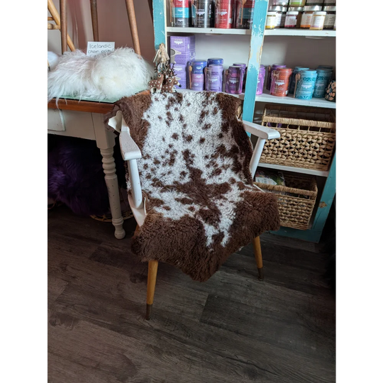 Brown and white highland spotted sheepskin grade a- draped over a vintage wooden chair with light legs