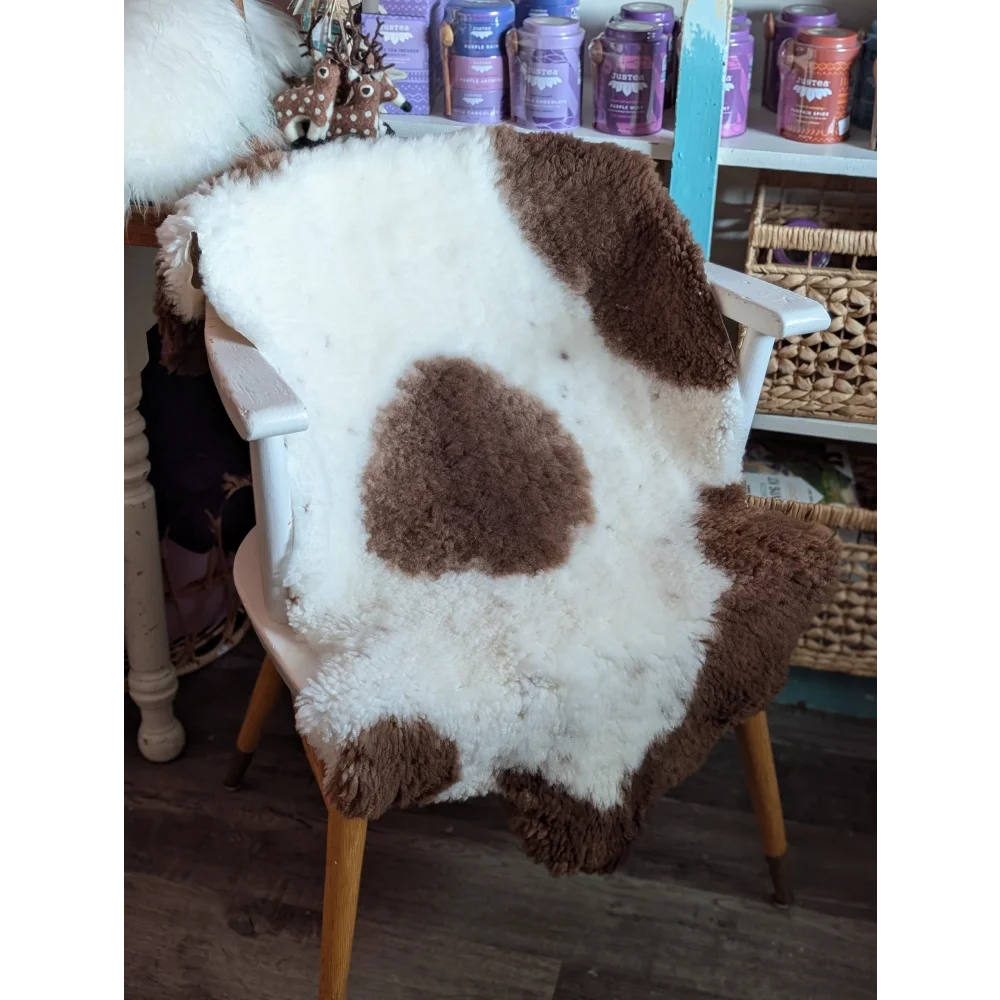 A cozy, grade a- highland spotted sheepskin rug with white and brown patches draped over a wooden chair