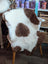 A cozy, grade a- highland spotted sheepskin rug with white and brown patches draped over a wooden chair