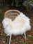A cozy natural white icelandic sheepskin long wool throw draped over a woven rattan chair with white legs