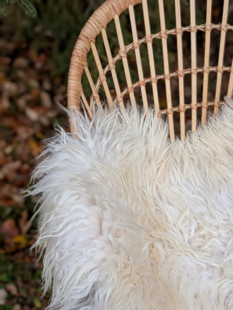 A large long wool natural white icelandic sheepskin throw draped over a woven wicker chair
