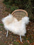A cozy natural white icelandic sheepskin with long wool draped over a woven rattan chair with white metal legs