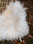 A large long wool natural white icelandic sheepskin draped over a woven chair showing plush curly texture