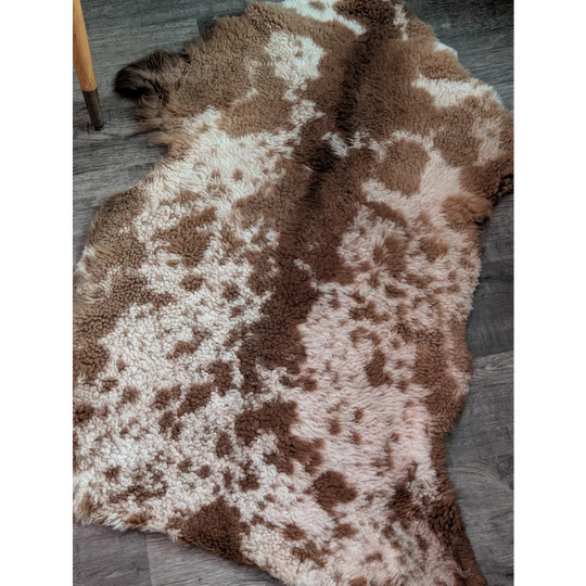 A plush grade a- highland spotted sheepskin rug with natural brown and cream speckled pattern in irregular shape