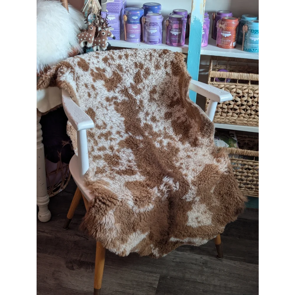 A cozy fluffy brown and white highland spotted grade a- sheepskin blanket draped over a wooden chair