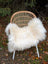 A plush natural white icelandic sheepskin long wool throw draped over a woven rattan chair with white metal legs