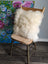 A plush off-white 16 x 16 merino sheepskin cushion cover with soft fluffy texture on a rustic wooden chair