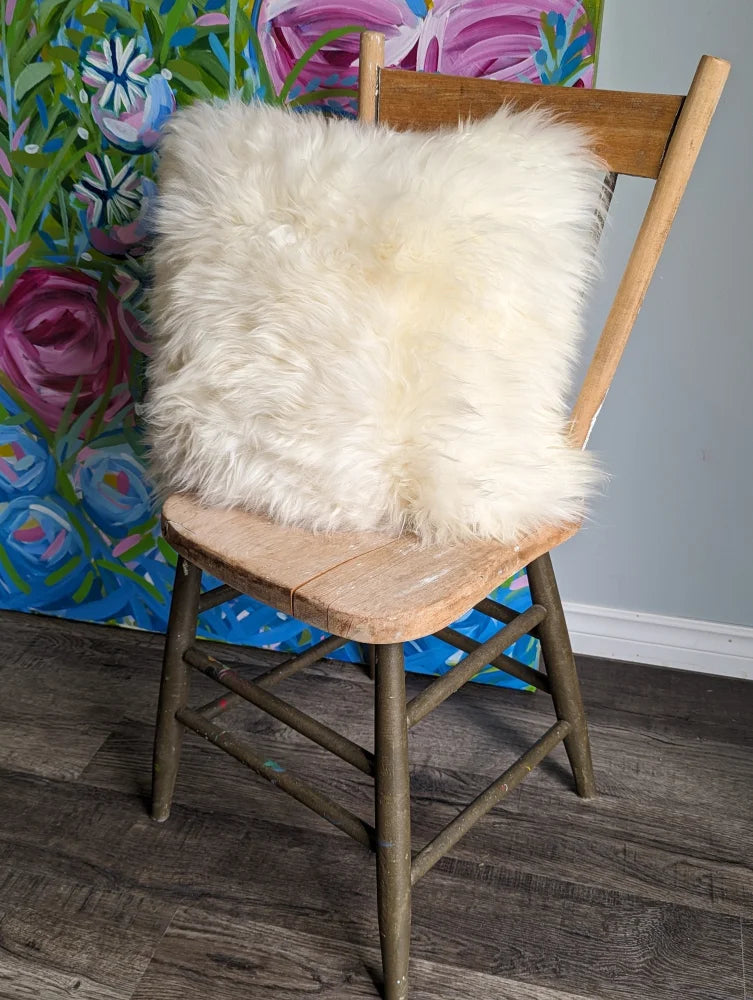 Cozy white merino sheepskin cushion on wooden chair with floral backdrop