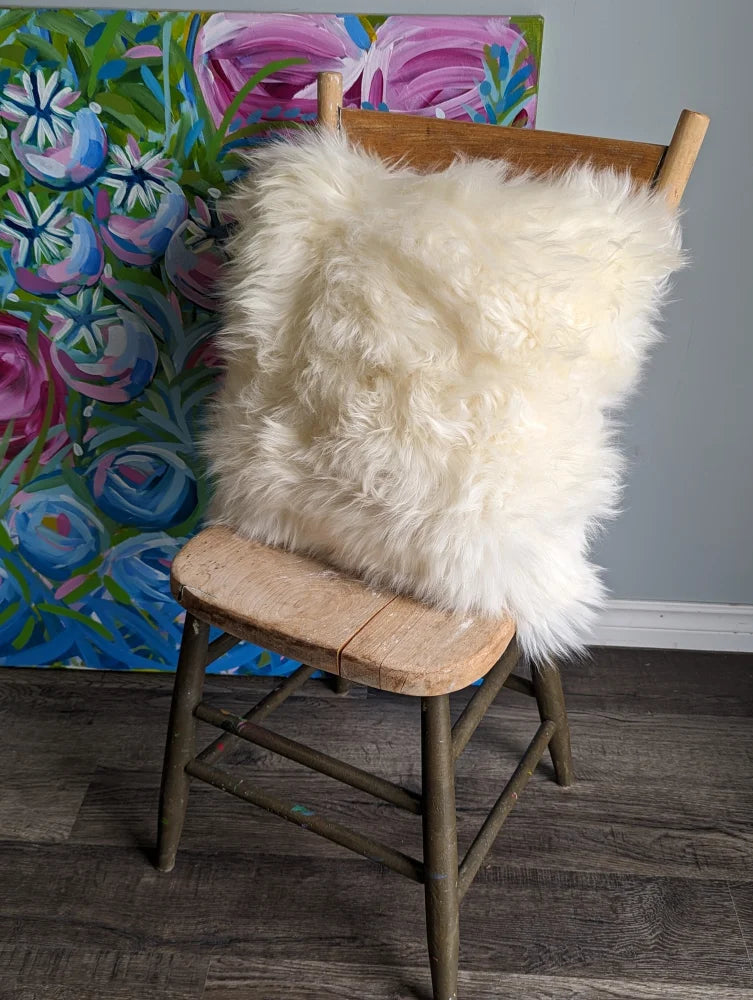 Cozy white sheepskin cushion on wooden chair with floral art background