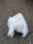 A fluffy natural white icelandic sheepskin with long wool draped over a rustic wooden chair