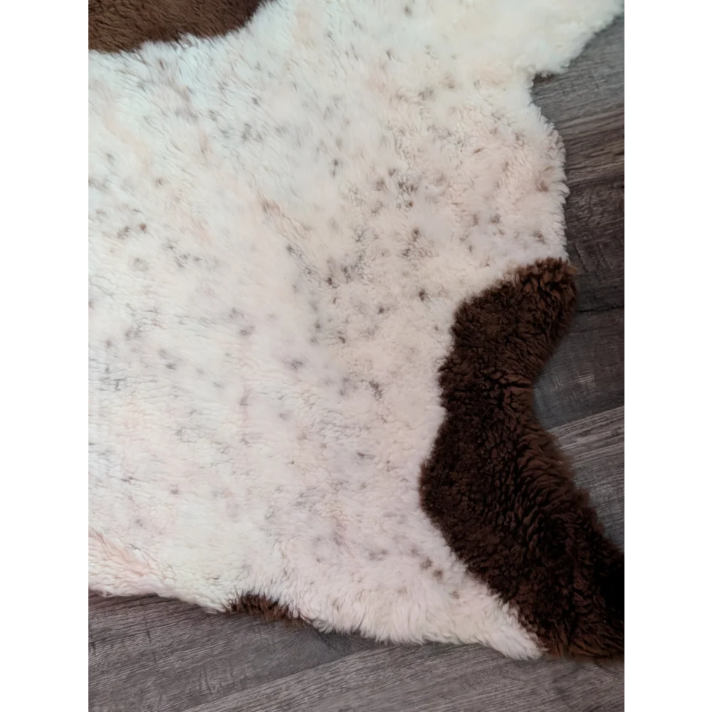 A plush cream-colored tibet highland spotted grade a- sheepskin rug with a natural brown patch and fluffy texture