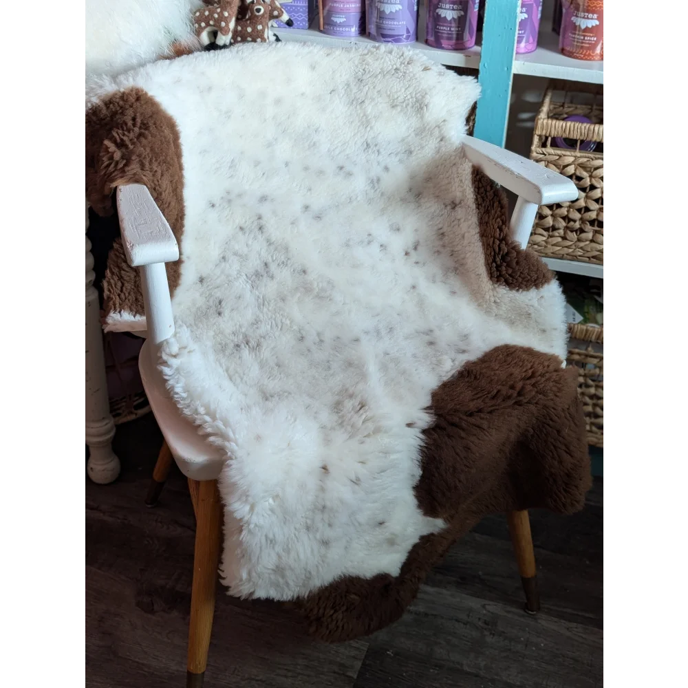 A cozy white and brown tibet highland spotted grade a- sheepskin throw draped over a wooden chair
