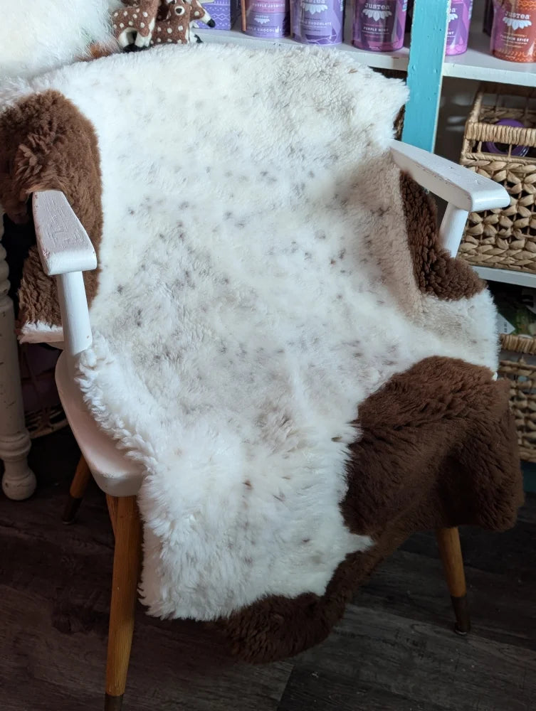 A cozy white and brown tibet highland spotted grade a- sheepskin throw draped over a wooden chair