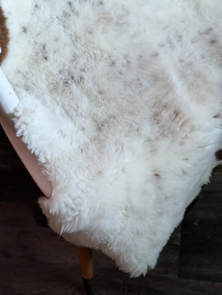 A plush white tibet highland spotted grade a- sheepskin rug with soft fluffy texture and subtle brown speckles