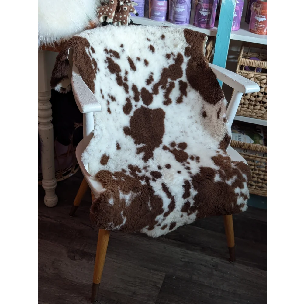 Brown and white tibet highland spotted grade a- sheepskin fur throw draped over a white wooden chair