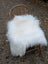 A plush natural white icelandic sheepskin long wool throw draped over a rustic wooden chair