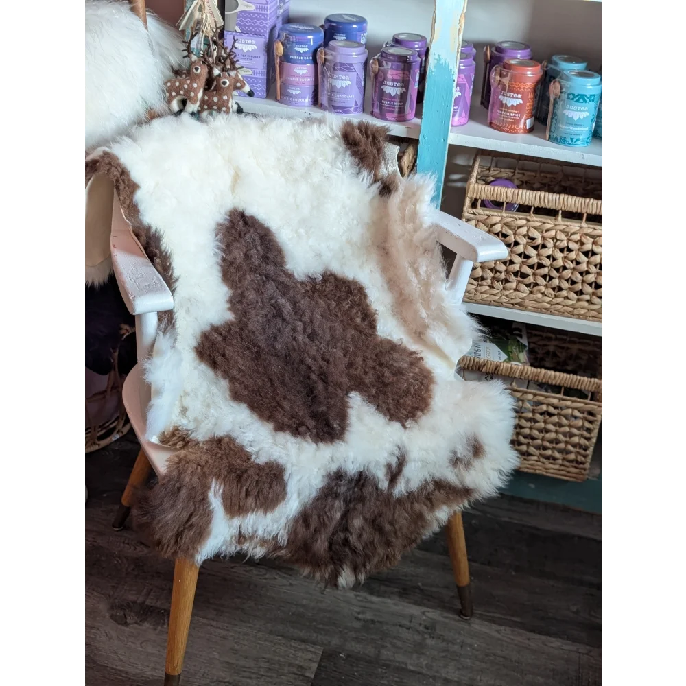 A fluffy brown and white tibet highland spotted grade a- sheepskin rug draped over a wooden chair
