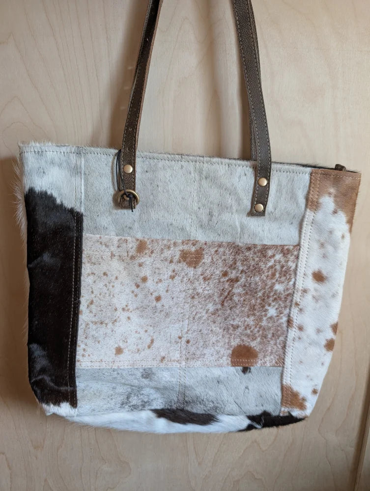A patchwork cowhide tote bag with brown black and white real cowhide panels stitched together for a stylish look