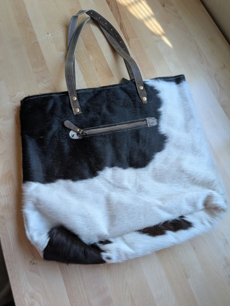 Black and white real cowhide tote bag with brown leather handles and metallic hardware from cowhide rugs collection