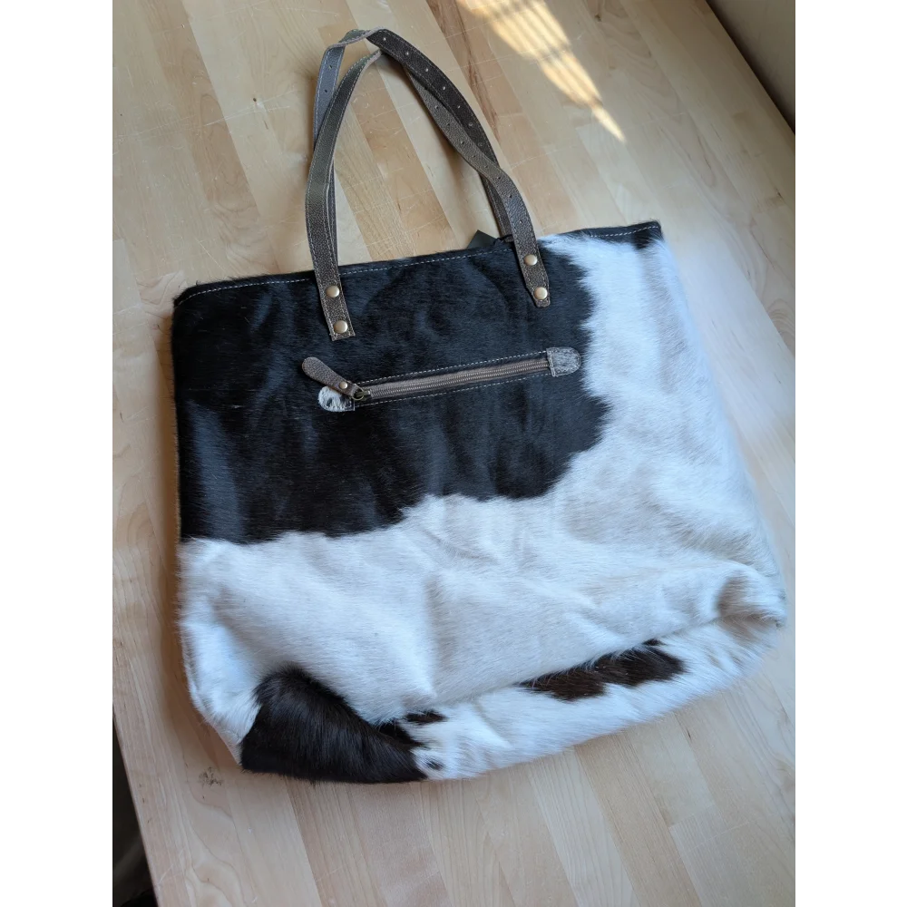 Black and white real cowhide tote bag with brown leather handles and metallic hardware from cowhide rugs collection