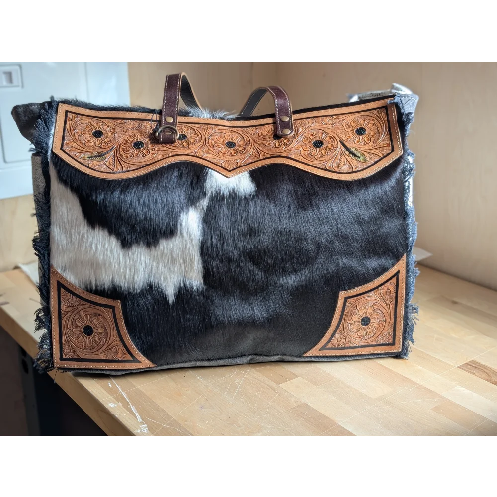 #2 the sunflower weekender bag is a black and white hair-on hide tote with tan cartwright hand-tooled floral accents and a zippered pocket