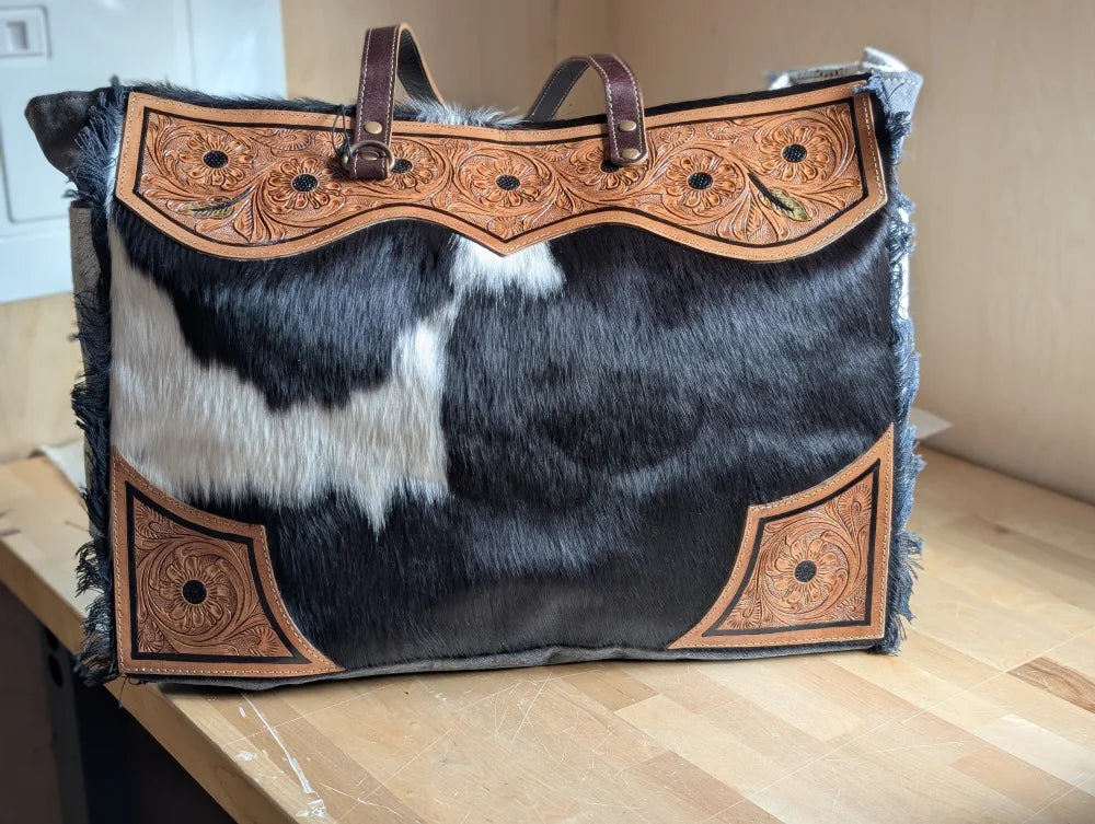#2 the sunflower weekender bag is a black and white hair-on hide tote with tan cartwright hand-tooled floral accents and a zippered pocket