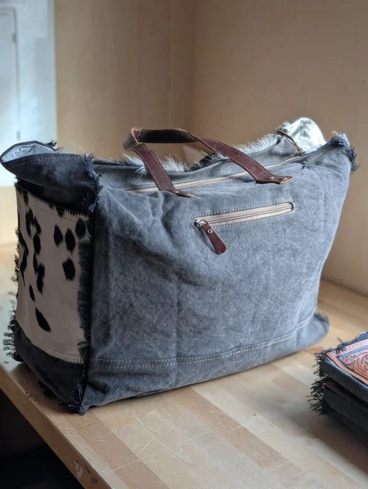 #2 the sunflower weekender bag is a gray canvas cartwright hand-tooled bag with brown leather handles and hair-on hide patch