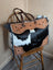 The sunflower weekender bag is a black and white hair-on hide tote with tan cartwright hand-tooled leather accents and a zippered pocket