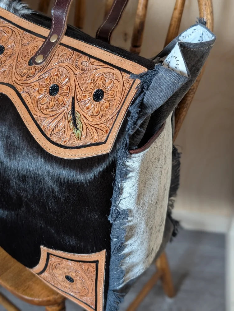 The sunflower weekender bag is a rustic cartwright hand-tooled bag with floral panels, black and white hair-on hide, and zippered pocket