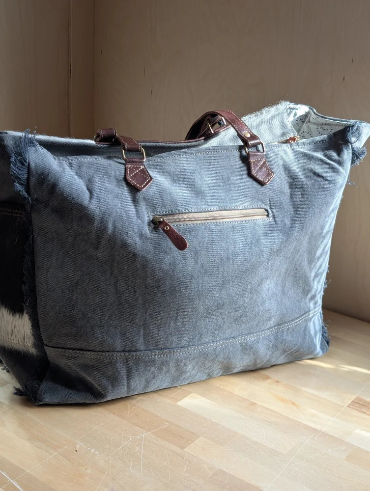 The sunflower weekender bag is a denim tote with frayed edges, brown leather handles, and a zippered pocket for easy access