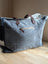 The sunflower weekender bag is a denim tote with frayed edges, brown leather handles, and a zippered pocket for easy access