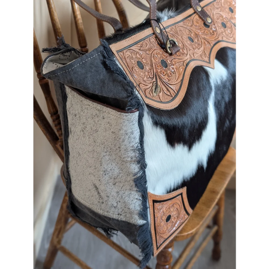 The sunflower weekender bag is a cartwright hand-tooled bag with hair-on hide cowhide, distressed denim, and zippered pocket