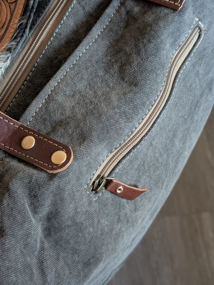 Gray canvas tote bag with brown leather accents and brass hardware featuring a zippered pocket for easy access