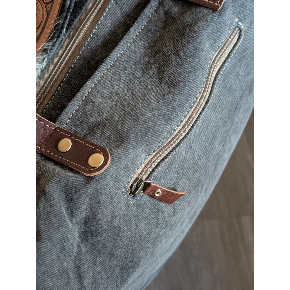 Gray canvas tote bag with brown leather accents and brass hardware featuring a zippered pocket for easy access