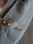 Gray canvas tote bag with brown leather accents and brass hardware featuring a zippered pocket for easy access