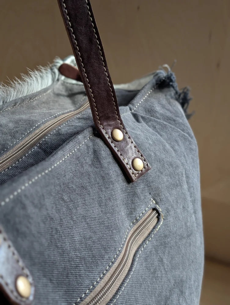 A distressed gray denim sunflower weekender bag with a brown leather strap and a zippered pocket detail