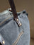 A distressed gray denim sunflower weekender bag with a brown leather strap and a zippered pocket detail