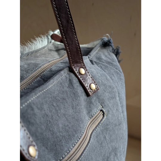A distressed gray denim sunflower weekender bag with a brown leather strap and a zippered pocket detail